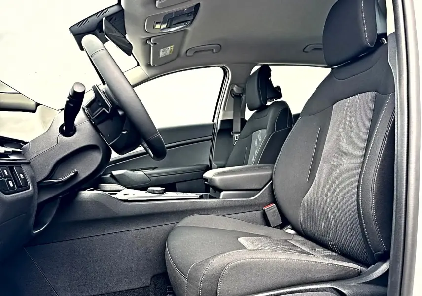 Vue intérieure côté conducteur du Kia Sportage hybride 2026, sièges noirs et accoudoir central avec rangement visible.
