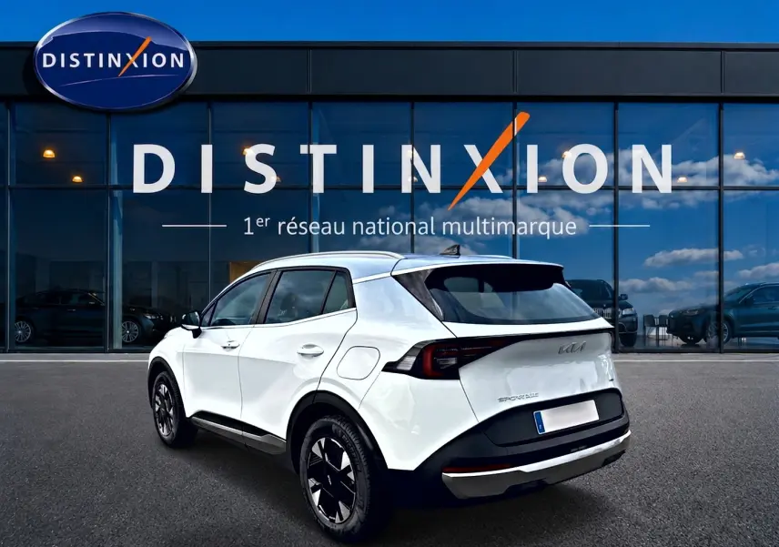 Vue 3/4 arrière droite d'un KIA Sportage blanc 2026 avec jantes alu noires et feux arrière LED distinctifs.