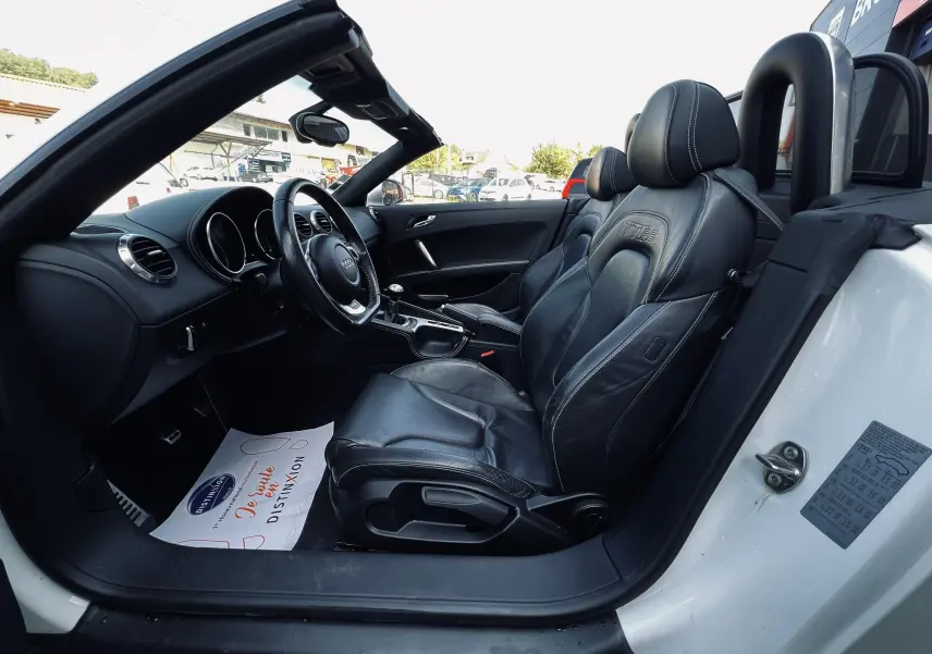 Vue intérieure côté conducteur de l'Audi TT RS Roadster blanc, sièges baquet cuir noir avec logo TT RS brodé.