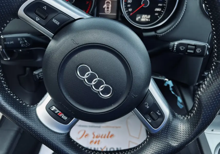 Gros plan sur le volant en cuir perforé de l'Audi TT RS Roadster avec logo Audi et badge RS visible.