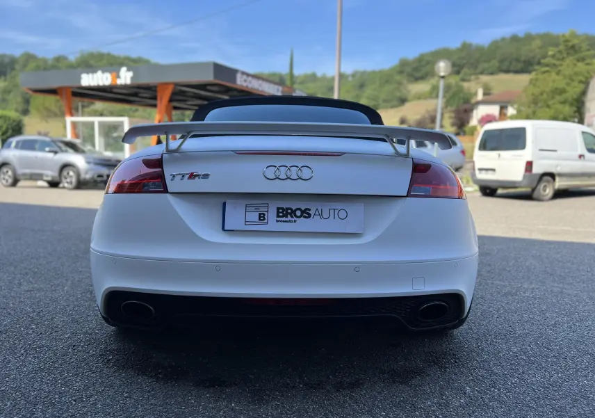 Vue arrière d'une Audi TT RS Roadster blanc avec aileron et double sortie d'échappement sur parking extérieur.