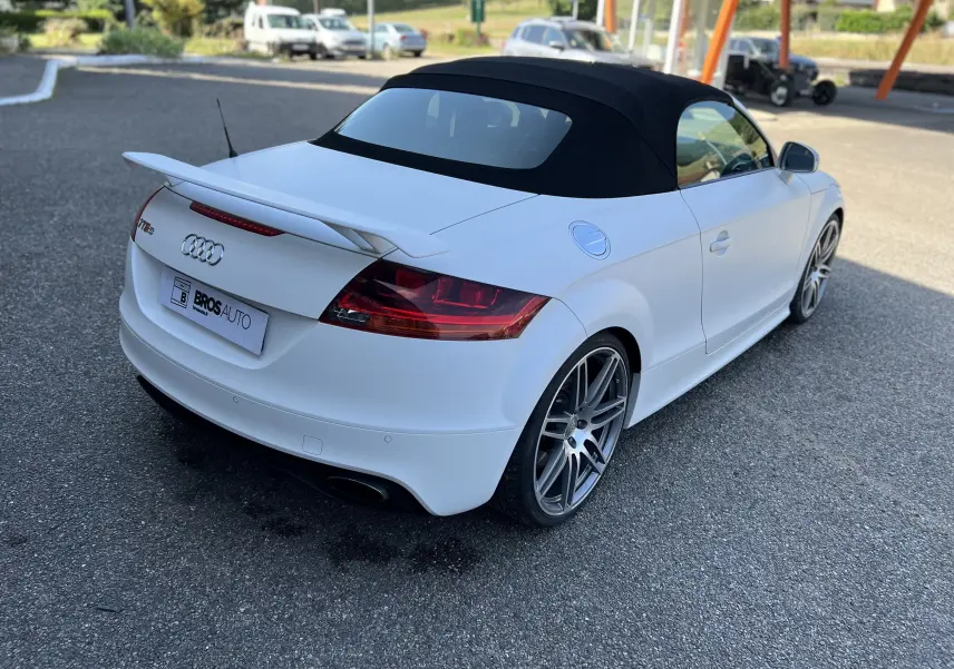 Audi TT RS Roadster blanc vue 3/4 arrière droit avec capote noire et aileron arrière distinctif.