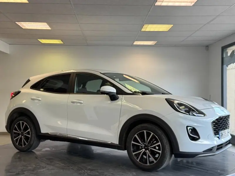 Ford Puma blanc Glacier vu de profil côté gauche, avec jantes noires et vitres arrière surteintées dans un showroom.