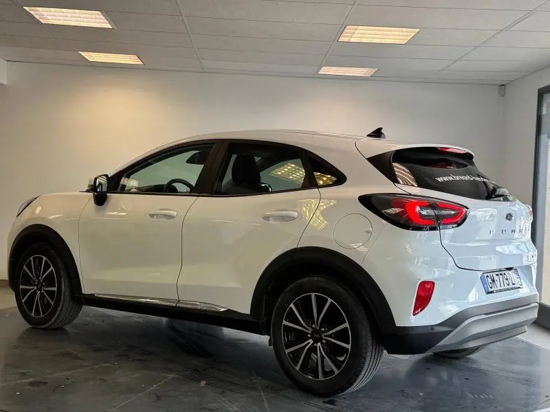 Ford Puma blanc glacier vu de profil côté gauche dans un showroom, avec jantes noires et vitres arrière surteintées.