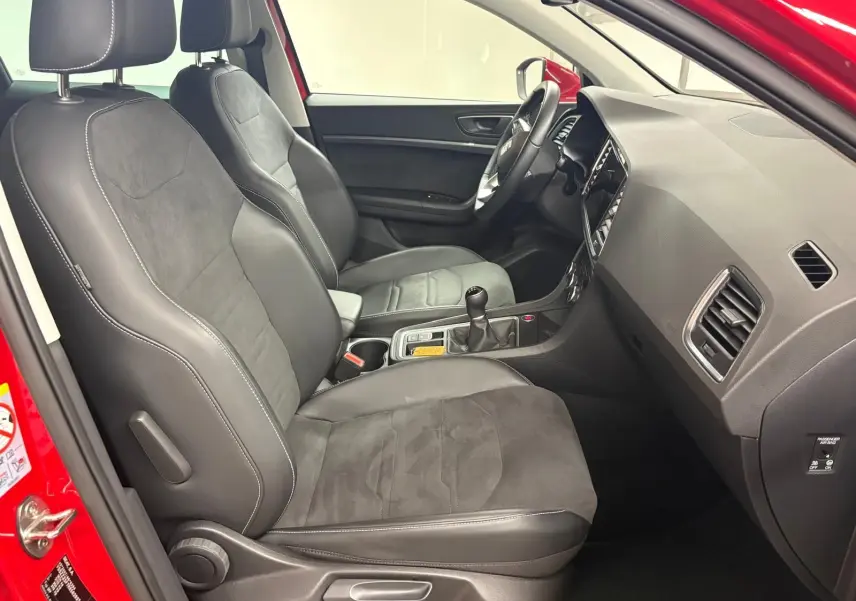 Vue intérieure côté conducteur du SEAT Ateca 2024 Rouge Velvet, avec sièges en cuir et alcantara, volant et levier de vitesses manuelle visibles.