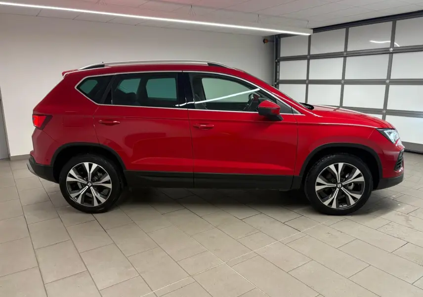 Vue de profil côté gauche d'un SEAT Ateca 2024 Rouge Velvet avec jantes alliage et barres de toit argentées.