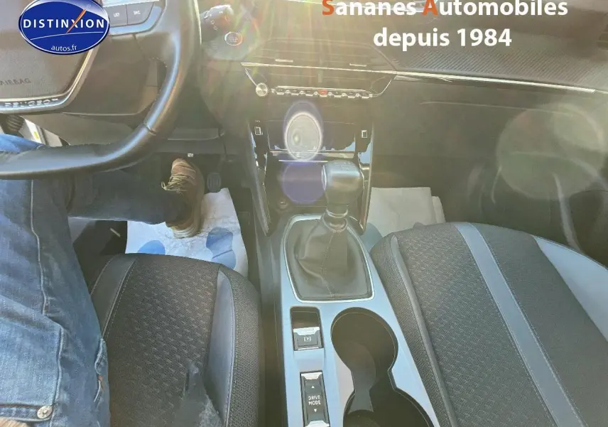Vue intérieure centrée sur la console centrale et levier de vitesse manuelle du Peugeot 2008 blanc, sièges tissu tri-matière.