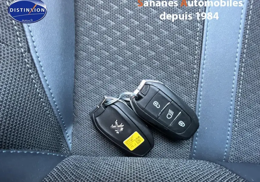 Gros plan sur deux clés mains libres Peugeot posées sur une sellerie tissu tri-matière bleu et noir.