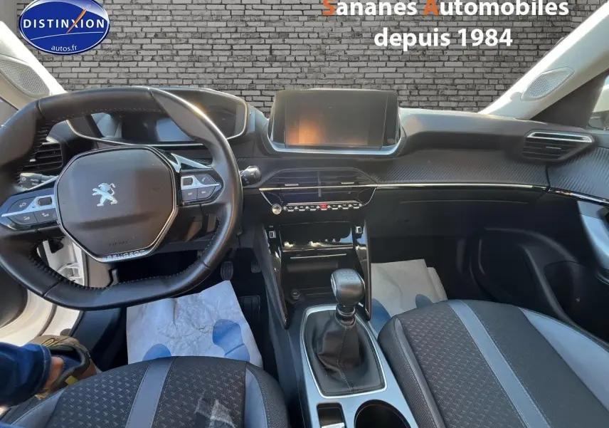 Vue intérieure avant du Peugeot 2008 blanc, mettant en valeur le volant, la console centrale et la sellerie tri-matière.