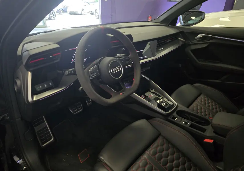 Intérieur noir de l'Audi RS3 Sportback 2023, vue côté conducteur, volant sport, sièges cuir avec surpiqûres rouges.