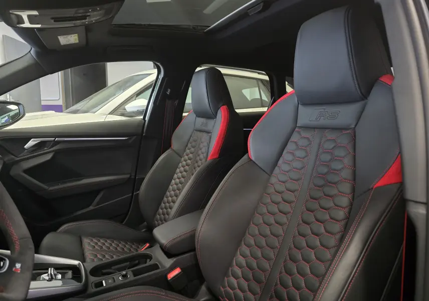 Vue intérieure côté conducteur de l'Audi RS3 Sportback 2023, sièges noirs avec surpiqûres rouges et logo RS embossé.