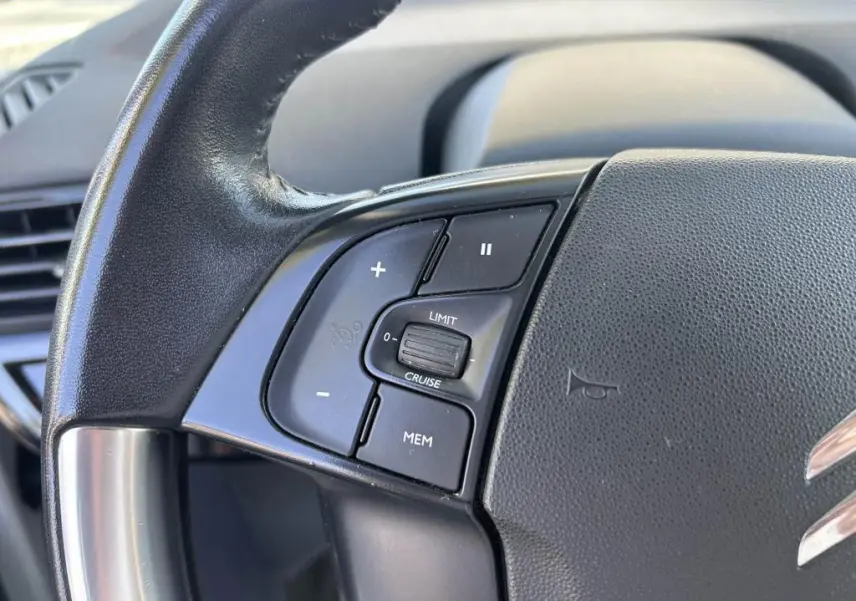 Gros plan sur les commandes de régulateur de vitesse à gauche du volant du Citroën Grand C4 Spacetourer beige clair.