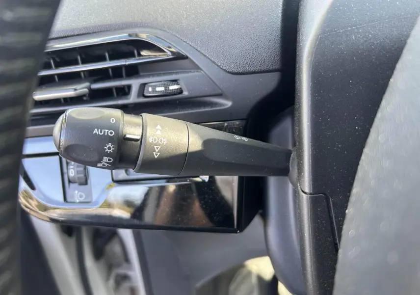 Gros plan sur la commande des phares et clignotants à gauche du volant dans le tableau de bord noir du Citroën Grand C4 Spacetourer beige clair.