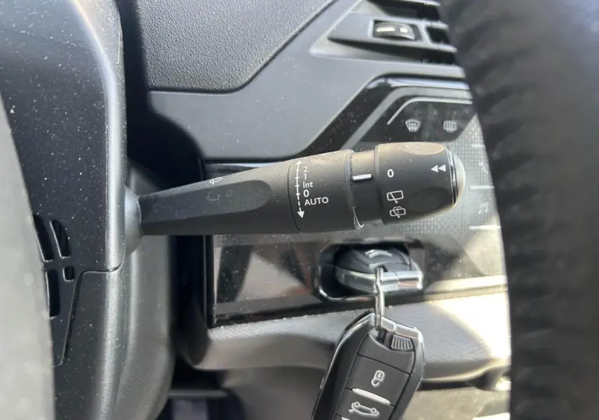 Gros plan sur la commande d'essuie-glace noire à gauche du volant dans l'habitacle sombre du Citroën Grand C4 Spacetourer.