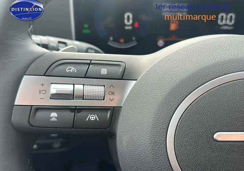 Gros plan sur les commandes multifonctions à gauche du volant cuir du Hyundai Tucson blanc Sérénité 2025 hybride.