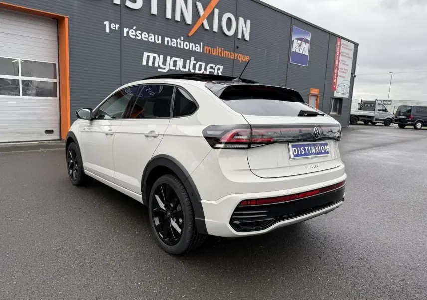 Vue 3/4 arrière droite d'un Volkswagen Taigo blanc avec jantes noires et vitres teintées sur parking.