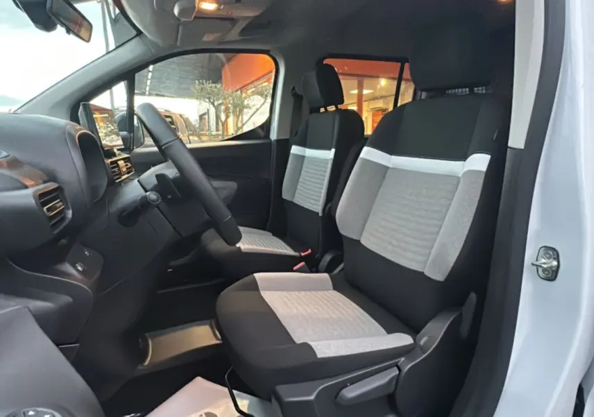 Vue intérieure côté conducteur du Citroën Berlingo 2026, sièges tissu bicolores gris et noir, volant multifonctions visible.