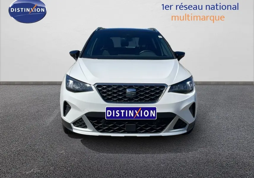 Vue frontale d'un SEAT Arona 2025 blanc à toit noir, avec calandre noire et phares LED allumés.