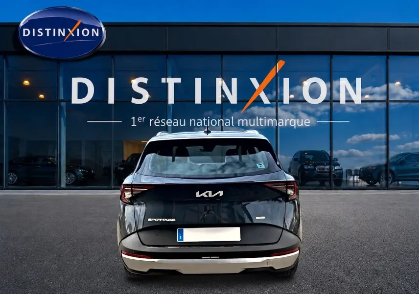Vue arrière d'un KIA Sportage gris eclipse 2026 garé devant une vitrine avec logo Distinxion.
