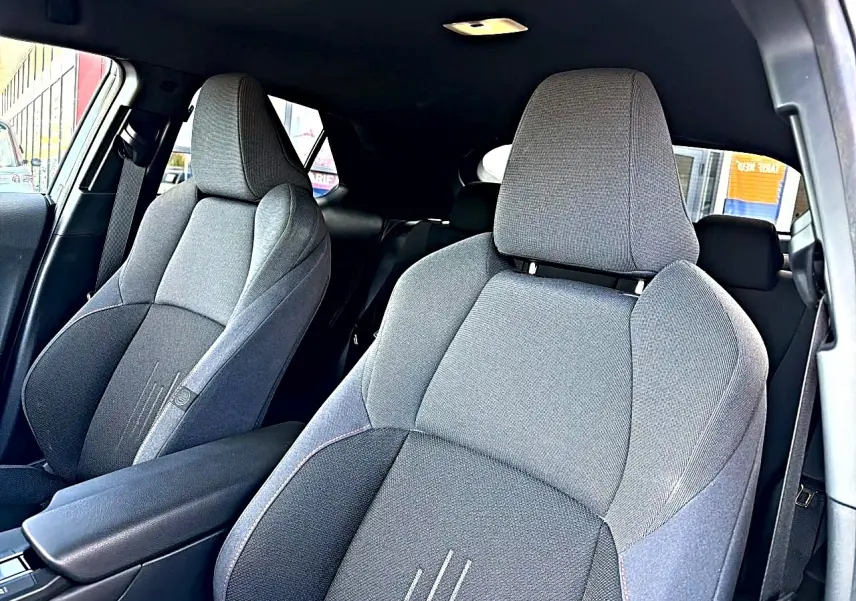 Vue intérieure des sièges avant gris foncé du Toyota C-HR 1.8 hybride 2025 avec accoudoir central et ceintures visibles.
