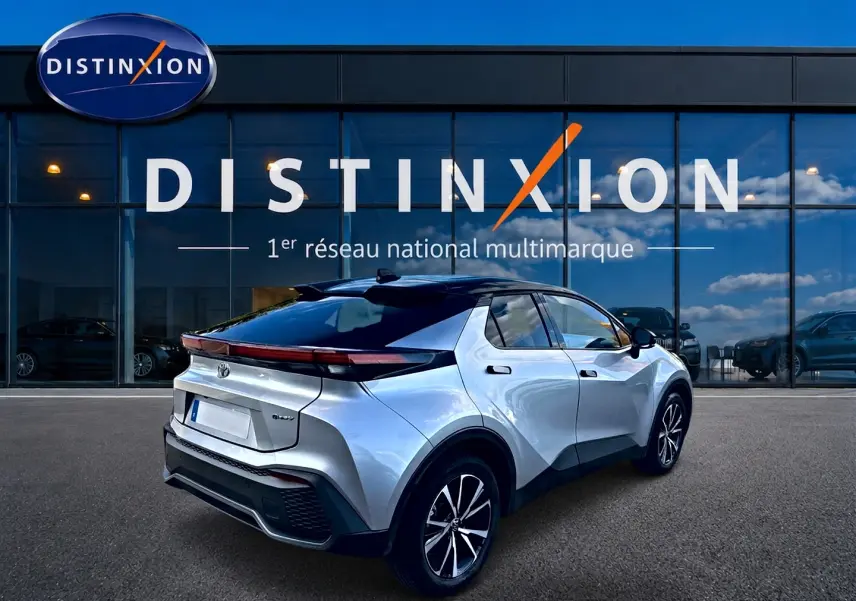 Toyota C-HR hybride gris en 3/4 arrière droit, avec toit noir et feux arrière LED continus, devant une vitrine Distinxion.