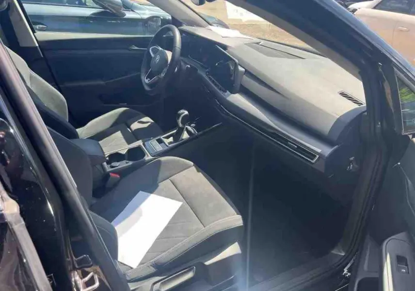 Vue intérieure côté conducteur d'une Volkswagen Golf VIII 1.5 TSI noire avec sellerie microfleece et tableau de bord moderne.