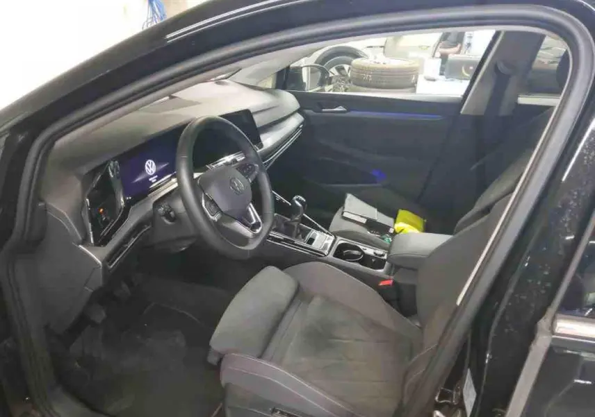 Vue intérieure côté conducteur de la Volkswagen Golf VIII Deep Black avec tableau de bord digital et sellerie microfleece noire.