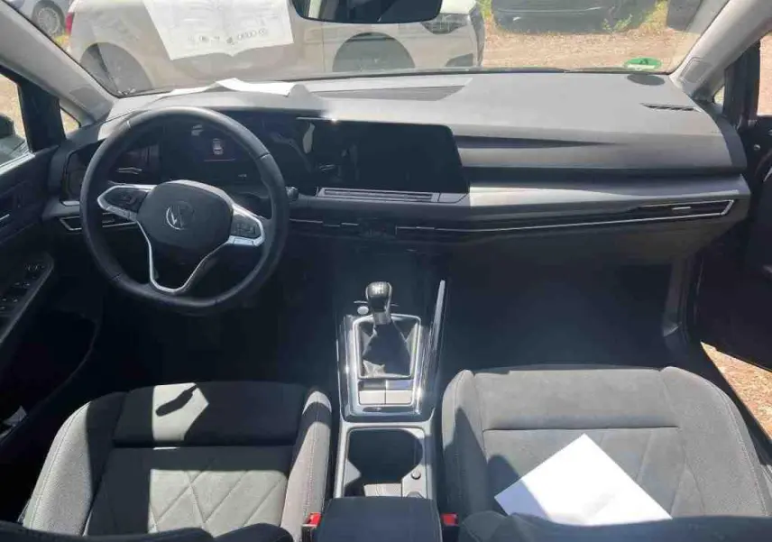 Vue intérieure avant de la Volkswagen Golf VIII 1.5 TSI noire, avec volant multifonction et boîte manuelle visible.