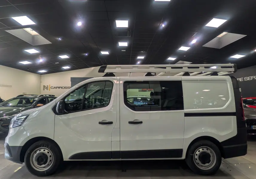 Vue de profil côté gauche du Renault Trafic Cabine Approfondie blanc minéral avec échelle sur le toit en intérieur showroom.