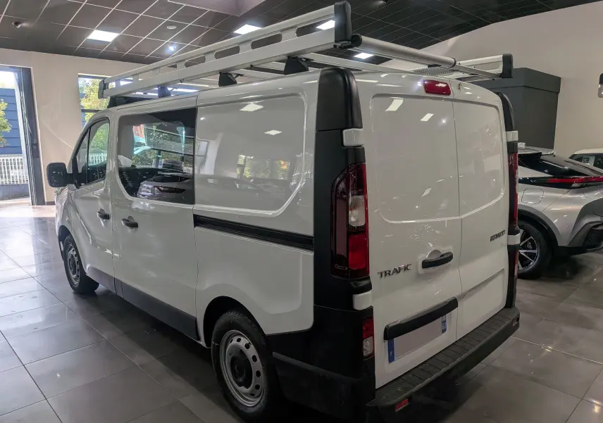 Vue 3/4 arrière droite d'un Renault Trafic Cabine Approfondie blanc minéral avec galerie de toit en intérieur showroom.