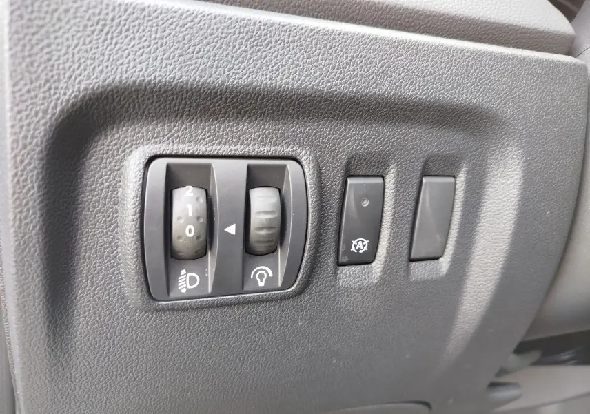Gros plan sur les commandes de réglage des phares et du tableau de bord, intérieur noir du Renault Captur Gris Cassiopée.