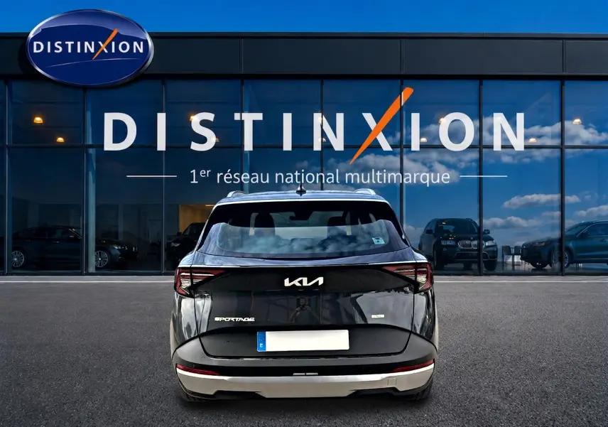 Vue arrière d'un Kia Sportage gris eclipse 2026 garé devant une vitrine avec logo Distinxion.