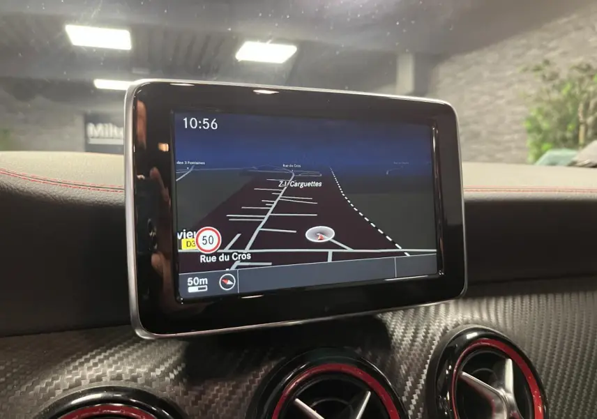 Écran GPS central avec carte, entouré de buses d'aération rouges sur tableau de bord carbone d'une Mercedes Classe A grise.