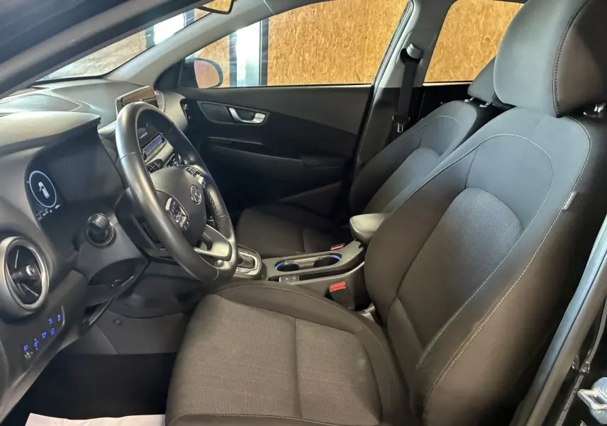 Vue intérieure côté conducteur du Hyundai Kona 1.6 GDI 140 Creative 2023 avec sièges tissu noir et volant multifonction.