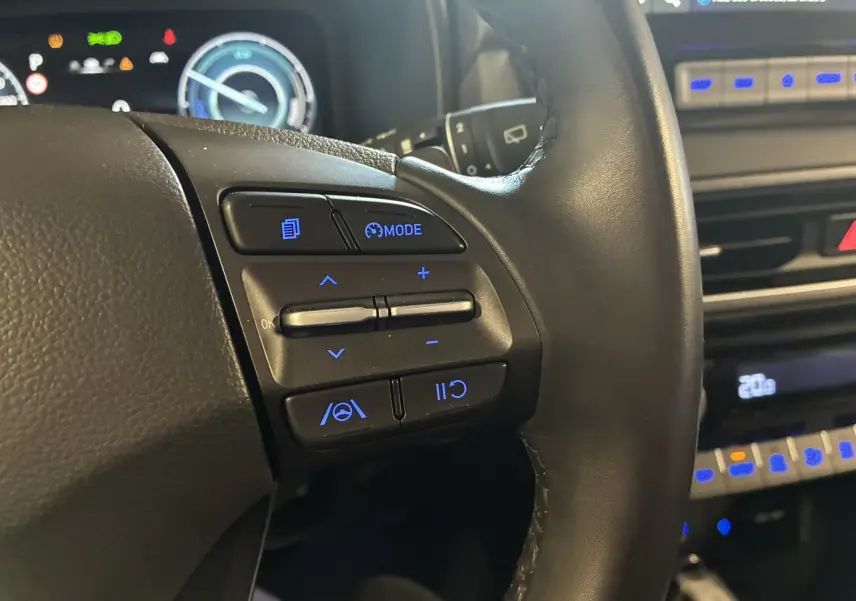 Gros plan sur les commandes de volant à gauche du Hyundai Kona noir 2023, avec éclairage bleu des boutons et tableau de bord visible.