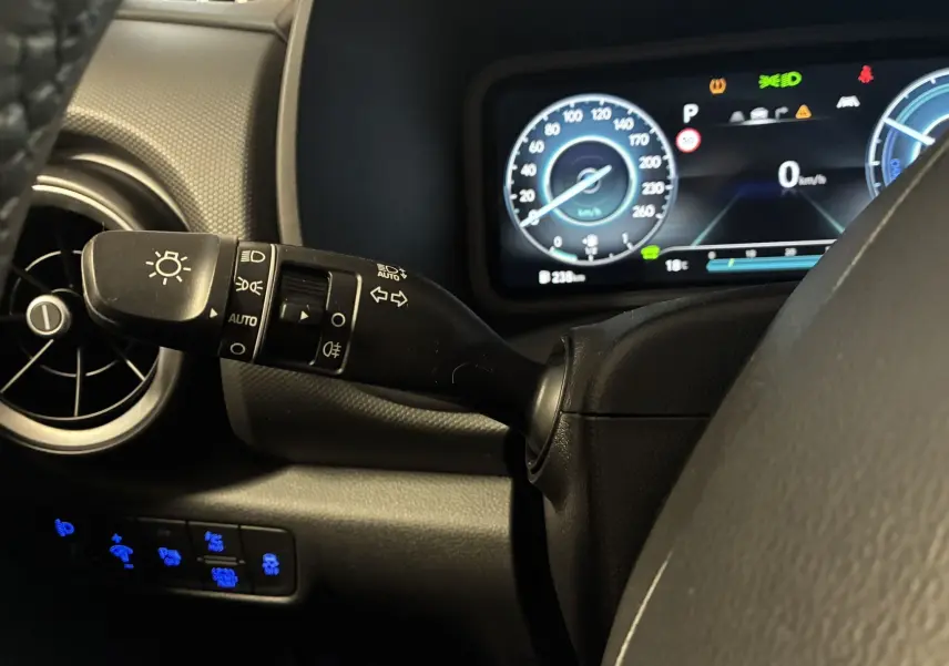 Gros plan sur le commodo des phares et le tableau de bord numérique du Hyundai Kona noir hybride 2023.