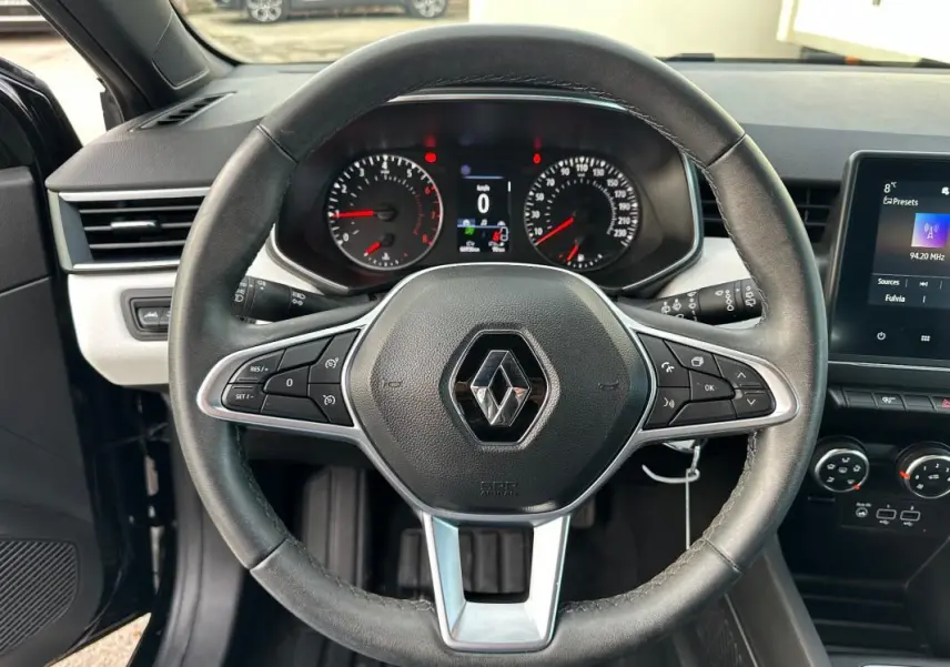 Vue intérieure centrée sur le volant noir de la Renault Clio V avec tableau de bord et écran tactile visibles.