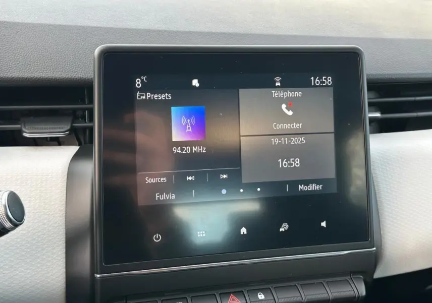 Écran tactile central de la Renault Clio V noire, affichant la radio FM et les options téléphone à 16h58.