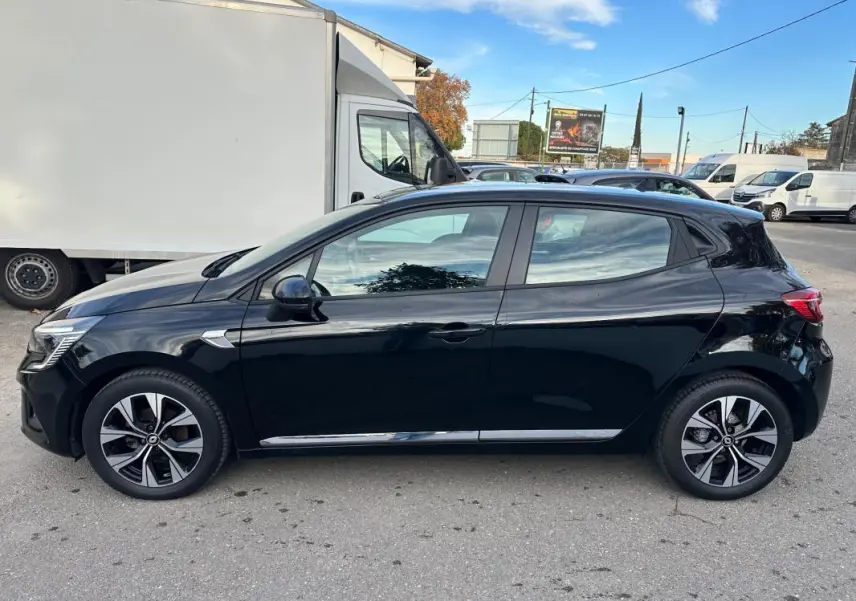Profil côté gauche d'une Renault Clio V noire avec jantes alliage 16 pouces, stationnée en extérieur par temps clair.