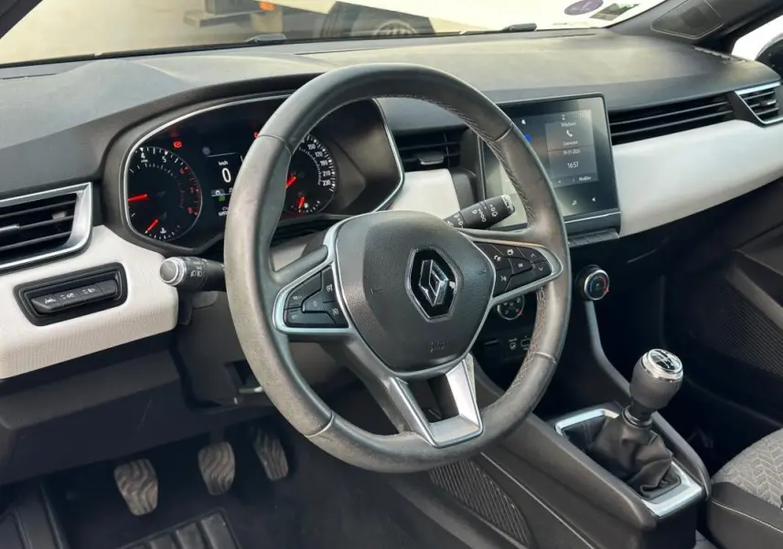 Vue intérieure côté conducteur de la Renault Clio V SCe 65 21 Limited avec volant cuir, tableau de bord digital et levier de vitesse manuel.