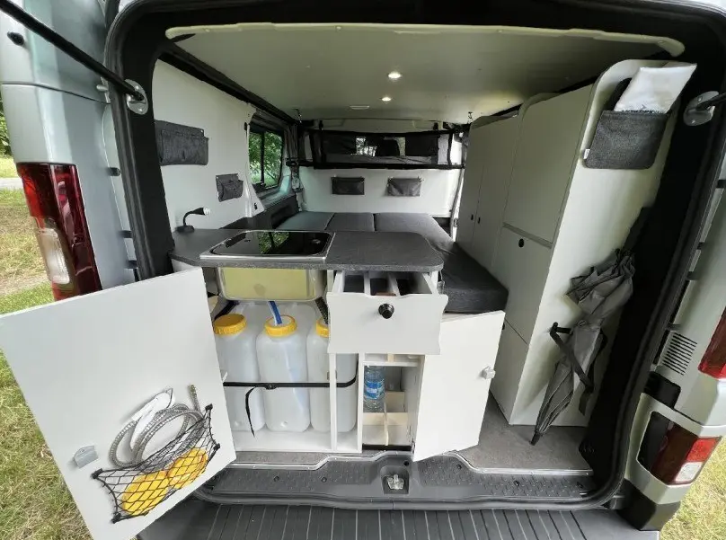 Vue arrière intérieure du Renault Trafic Fourgon gris 2025 aménagé avec kitchenette, rangements et couchage.