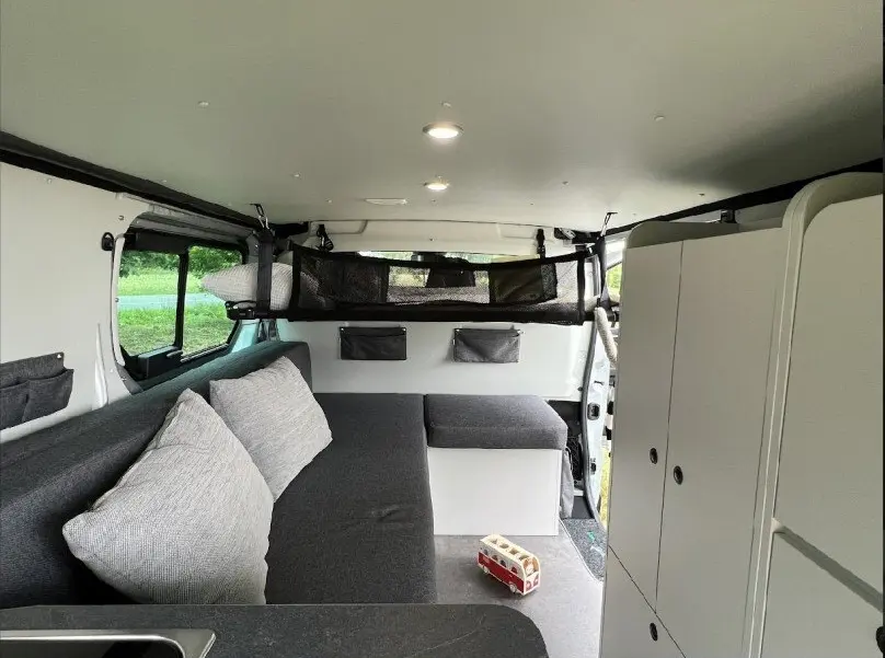 Intérieur du Renault Trafic Fourgon aménagé, vue de côté droit montrant banquette grise et rangements blancs.