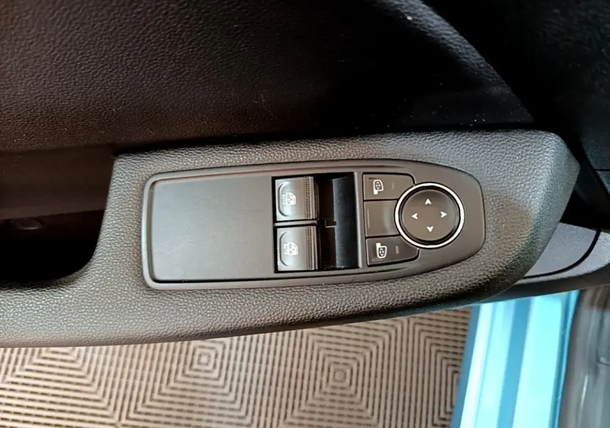 Vue rapprochée des commandes de réglage des vitres et des rétroviseurs sur la porte côté conducteur d'une Renault Clio bleu.