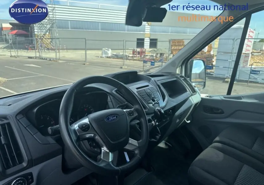 Vue intérieure du poste de conduite du Ford Transit Fourgon blanc, montrant le volant multifonction et la console centrale.