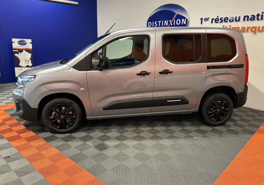 Profil côté gauche du Citroën Berlingo Multispace gris Artense avec jantes noires dans un showroom.