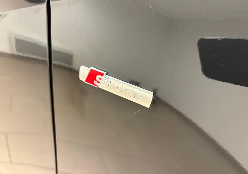 Gros plan sur l'emblème S line argent et rouge sur la porte noire métallisée d'un Audi Q2 35 TFSI 2026.