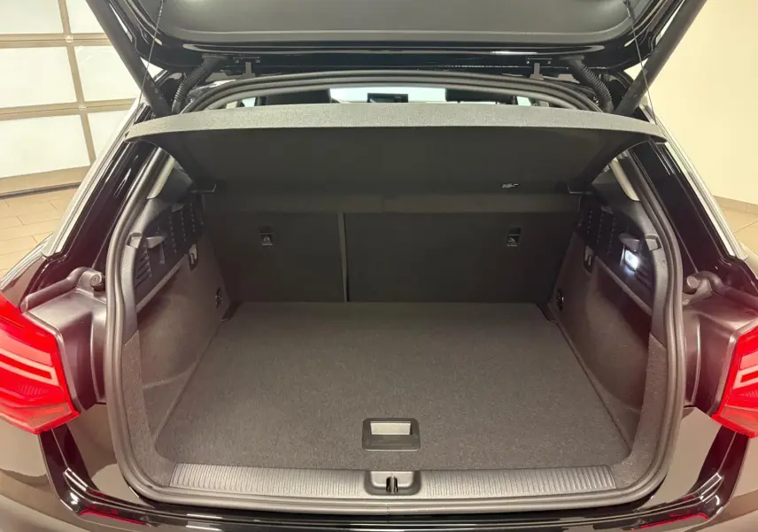 Coffre ouvert vu de l'arrière d'un Audi Q2 35 TFSI S Line noir Mythic, montrant l'espace de chargement vide et l'éclairage intérieur.