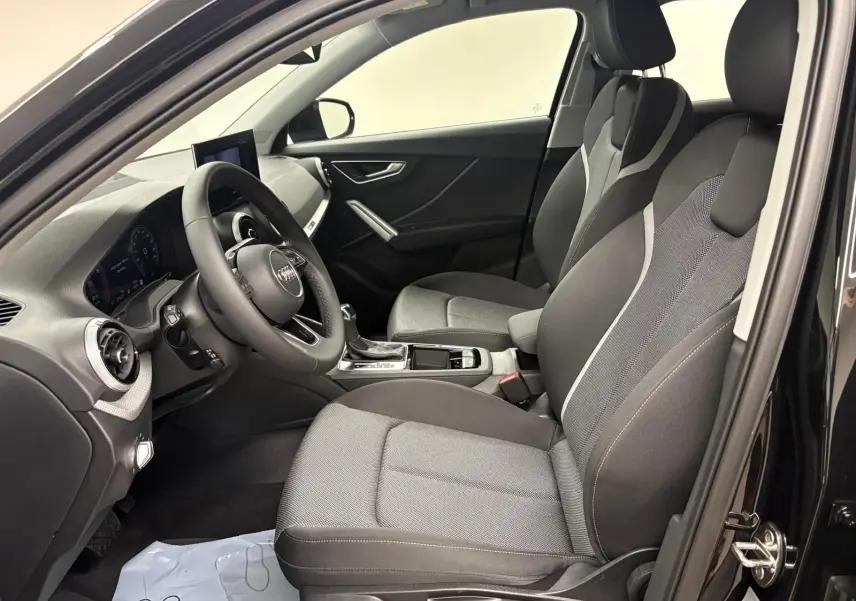 Vue intérieure côté conducteur de l'Audi Q2 35 TFSI S Line 2026 en Noir Mythic, sièges avant en tissu gris et noir.