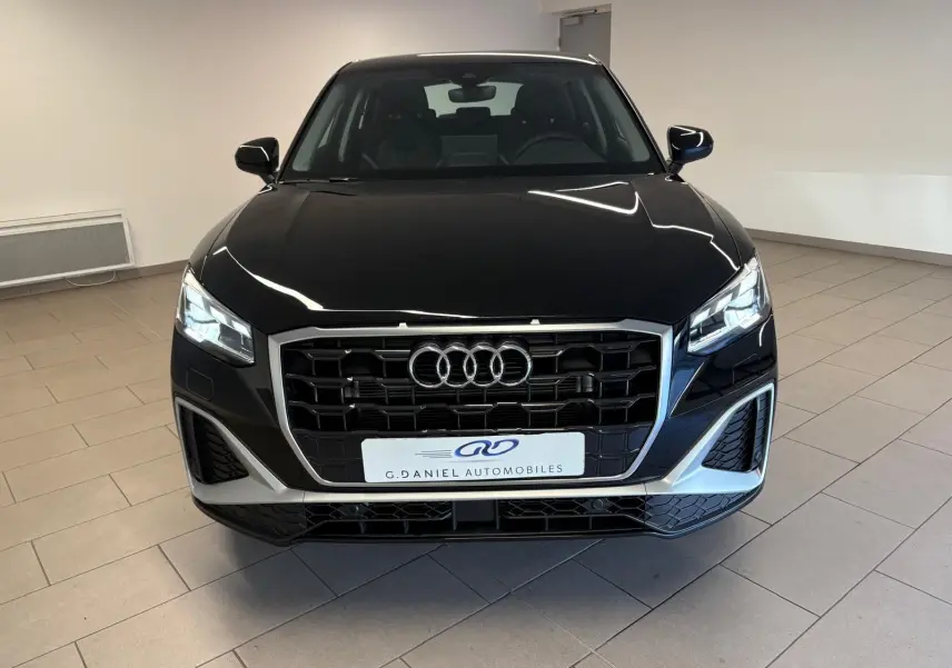 Vue avant d'un Audi Q2 35 TFSI S Line noir mythic avec calandre large et phares LED allumés en intérieur.
