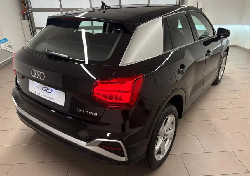 Audi Q2 35 TFSI noir mythic vue 3/4 arrière droit, avec toit contrastant gris et feux arrière allumés.